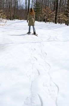 Woman walking in snow shoes in winter forest.