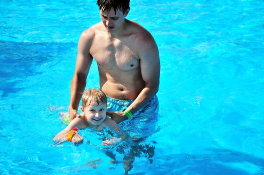 father teaching little boy to swim in the waterpool