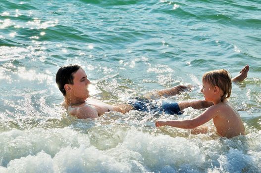 father and son  squattering  in waves of sea. backlight