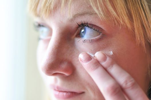 face of girl applying cosmetic cream on skin around eyes - soft focus
