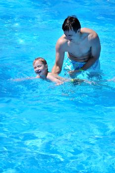 futher and son having fun in swimming pool, son is trying to swim