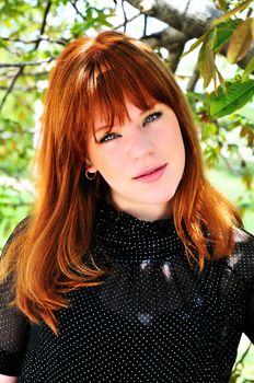 redheaded girl is standing under the tree and smiling
