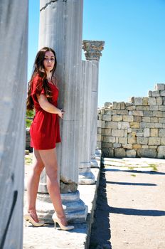 Young fashion model wearing only sexy red tunic and high-heel shoes standing close to the Ancient Ruins
