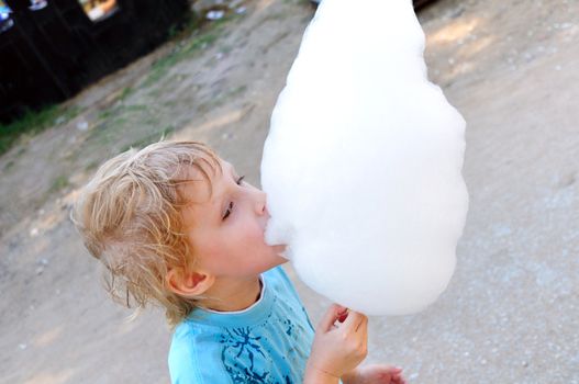 little boy is enjoying cotton candy in hot summer day
