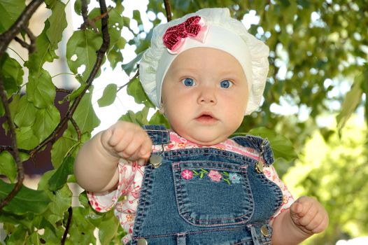 Pretty little girl play with green trees branchlets.