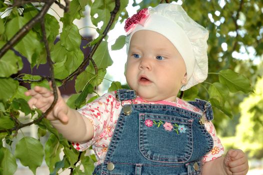 Pretty little girl play with green trees branchlets.