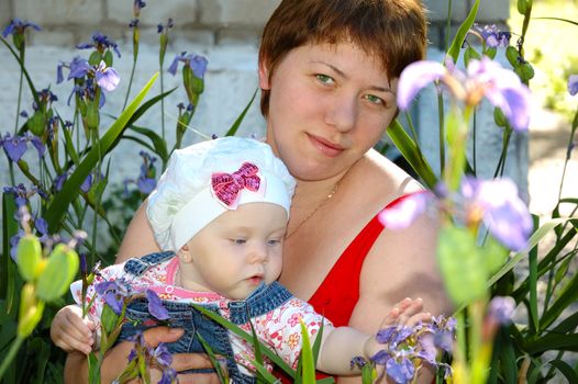 Pretty little girl and her mother sitting in iris flowers.