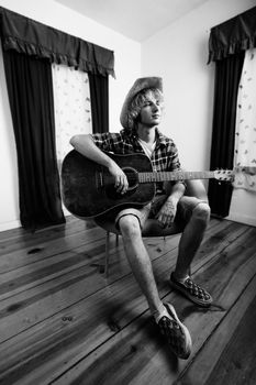 Young musician with an old guitar in an empty room