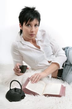 young woman reading a book and drinking tee