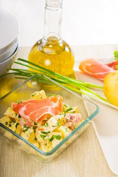 fresh home made parma ham and potato salad,with raw ingredients around with bowls and dishware on a table