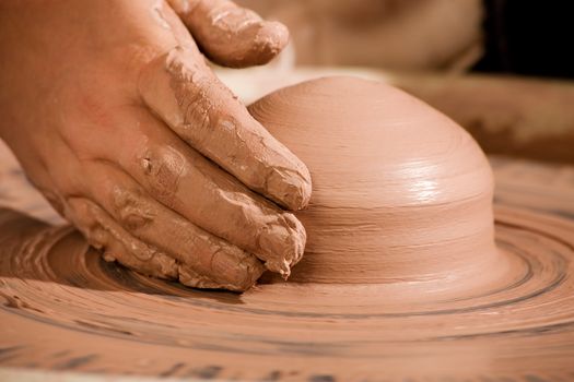 Hand shaping wedge of clay on spinning potters wheel