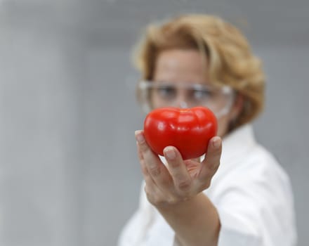 Image of a female researcher offering a tomato and an apple to suggest the idea that healthy eating is recommended also by scientists.Specific lighting for a classical research laboratory.