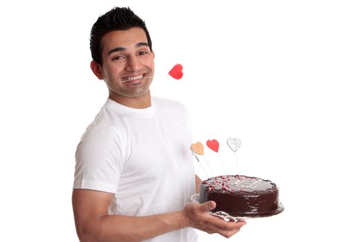 A man holds a chocolate mud cake decorated with love hearts.   He has a red love heart clenched between his teeth.  Suitable for birthday or special occasion.