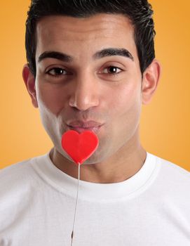 A flirtatious man kissing an edible red love heart on a stick
