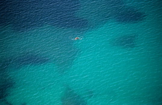 A solitary swimmer paddles in the Mediterranean sea.