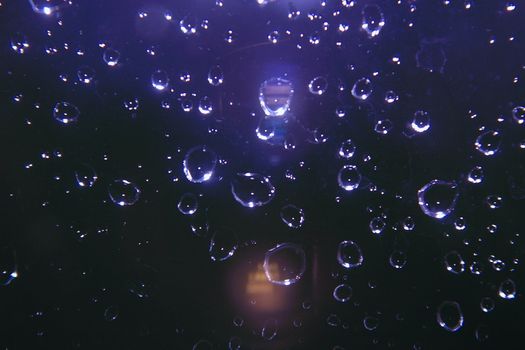 sparkling rain drops on glass against a dark background