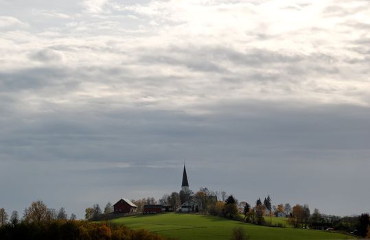 Church spire on a hill against the dark moody sky of an approaching storm front. The church is located in Fet, Norway.
