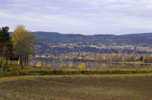 An autumn Norwegian landscaspe. A bare field by the Glomma river, with autumn-coloured hills on the other bank.
