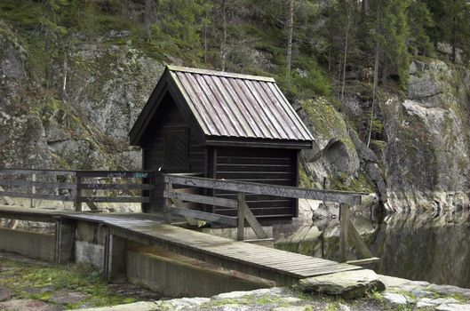 A small house over a watergate on a lake dam.
