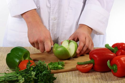 The cook with vegetables cuts an apple on a kitchen board.