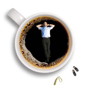 Top view of a young business man taking a nap inside an isolated cup of coffee with his tie and shoes sitting aside.