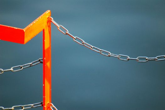a chain of orange fence in front of blue water