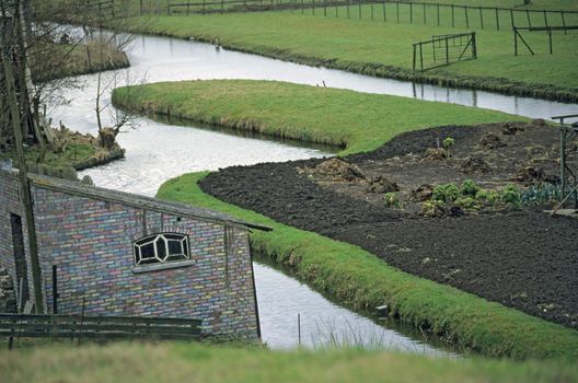 A colourful shed sits by a canal and a garden being prepared for planting.