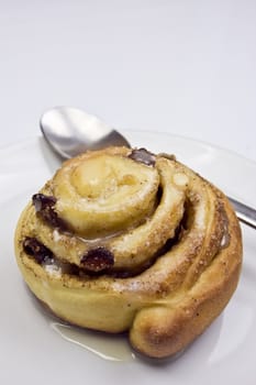 Homemade cinnamon bun in a plate with tea spoon.