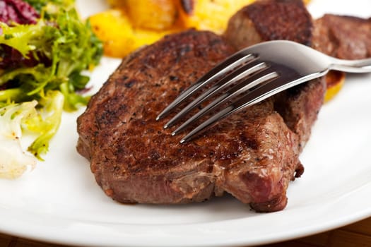 silver fork on a steak with salad and potatoes