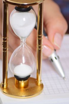 Female hand with pen and sand clock removed close up