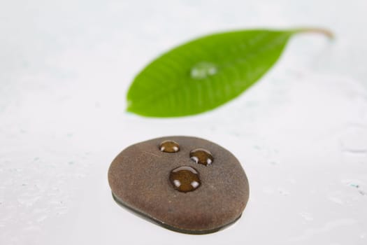 Stone for spa with three drops on wet glass removed close up against green sheet