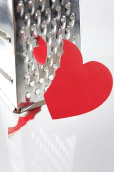 Fragmentary paper heart against a kitchen grater removed close up