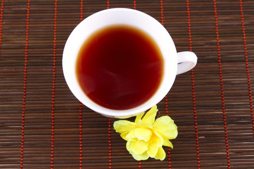 Cup of tea with a yellow flower on a bamboo napkin removed close up