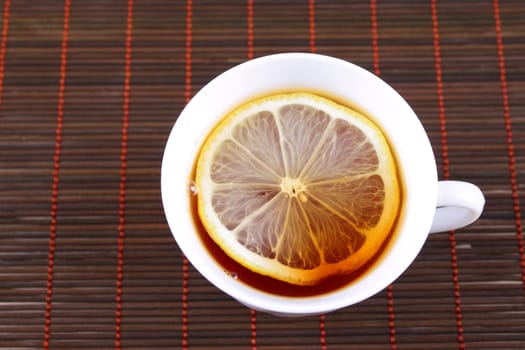 Cup of tea with a lemon on a bamboo napkin removed from above close up