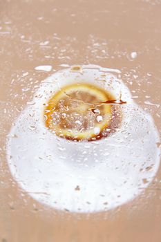 Cup of tea with a lemon behind glass splashed with water drops
