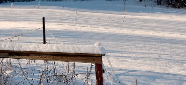 Crystallised snow on a wooden rail with snow-covered field behind.
