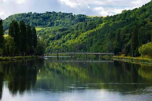 Hills, forest and bridge with reflection in river in summer