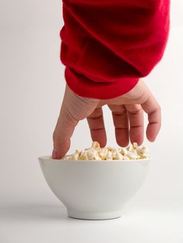 A hand trying to reach some popcorns from a bowl.