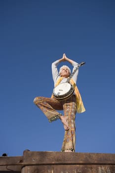 Banjo player standing in a Yoga pose against the blue sky