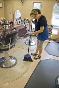 A hairdresser working in the salon sweeps up after her last client.