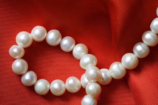 Closeup of pearl necklace lying on red textile background