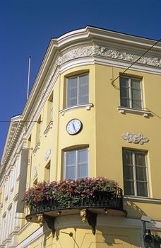 A yellow building on a corner with beautiful flowers and a clock. Helsinki, Finland. 