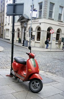 A red-orange scooter is parked on a sidewalk in Dublin, Ireland