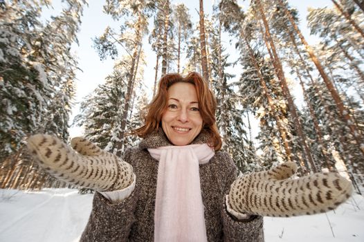 Smiling red-haired woman having fun on winters day in forest.