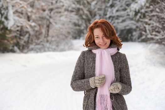 Smiling red-haired woman having fun on winters day in forest.