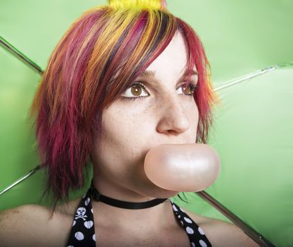 Closeup woman in front of a green umbrella blowing a bubble