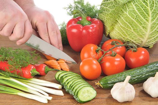 Hands cut a knife a carrot among vegetables on board