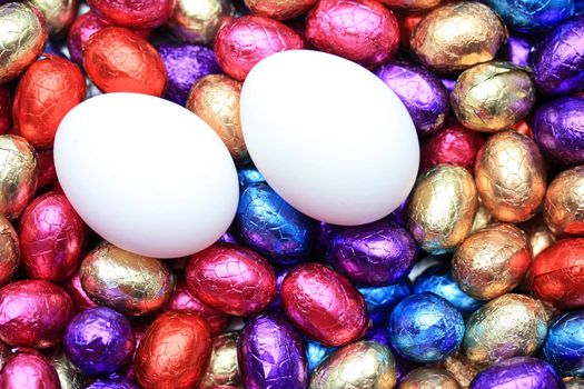 Two white chicken eggs in a group of chocolate easter eggs