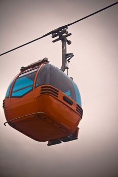 New orange mountain gondola suspended from wire against white sky with vignette