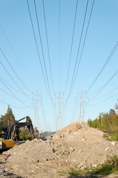 Three power masts supporting high voltage lines with a construction site and an excavator beneath
